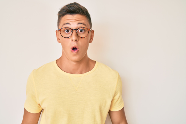 Junger hispanischer Junge in lässiger Kleidung und Brille erschrocken und erstaunt mit offenem Mund für Überraschung, ungläubiges Gesicht  - Foto, Bild