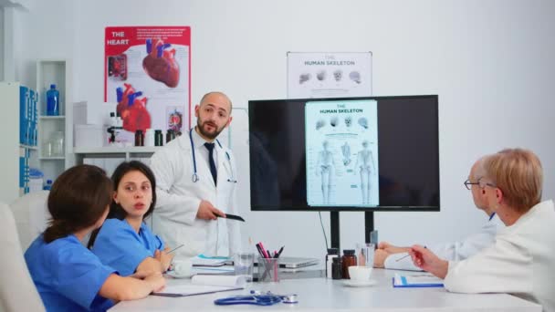 Опытный человек врач анализирует изображение скелета человека с коллегами - Кадры, видео