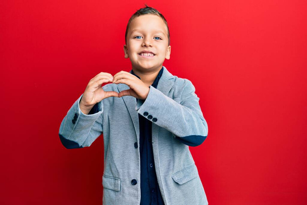 Little kid boy wearing elegant business jacket smiling in love doing heart symbol shape with hands. romantic concept.  - Photo, Image