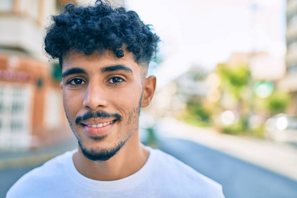 Jonge Arabier man lachend gelukkig kijkend naar de camera op straat van de stad. - Foto, afbeelding