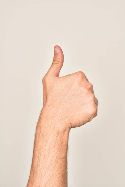 Mão de jovem caucasiano mostrando dedos sobre fundo branco isolado fazendo gesto de aprovação bem sucedida com polegares para cima, validação e símbolo positivo - Foto, Imagem