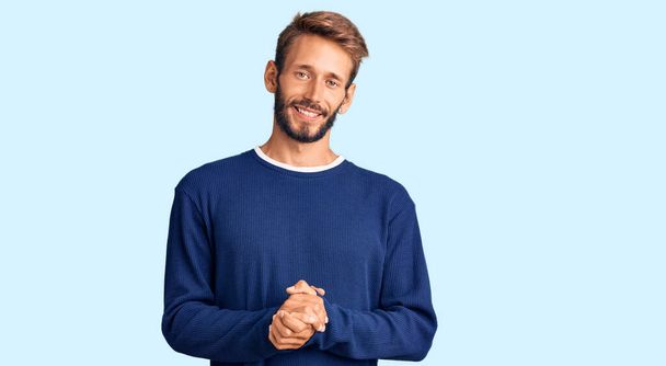 Hombre guapo rubio con barba vistiendo suéter casual con las manos juntas y dedos cruzados sonriendo relajado y alegre. éxito y optimismo  - Foto, imagen