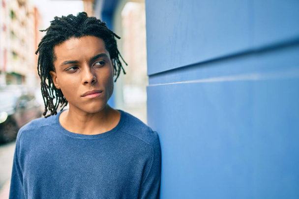 Şehrin sokağında duvara yaslanmış, ciddi bir suratı olan Afro-Amerikalı genç bir adam.. - Fotoğraf, Görsel