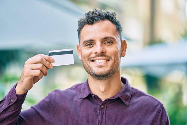 Genç İspanyol adam gülümsüyor, şehirde kredi kartı tutarken mutlu.. - Fotoğraf, Görsel