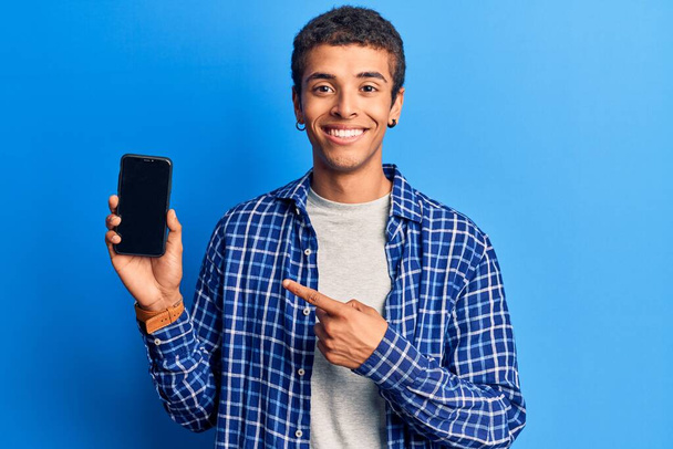Young african amercian man holding smartphone showing screen smiling happy pointing with hand and finger  - Фото, зображення