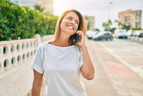 Beautiful middle age hispanic woman smiling speaking on the phone happy outdoors - Photo, Image