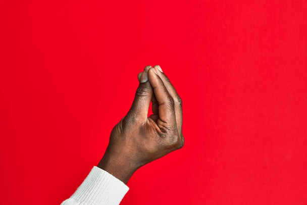 Brazo y mano del joven negro afroamericano sobre fondo rojo aislado haciendo gesto italiano con los dedos juntos, movimiento de gesto de comunicación  - Foto, Imagen