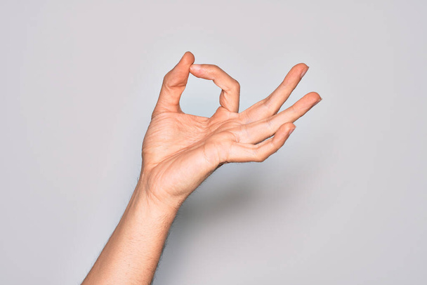 Hand of caucasian young man showing fingers over isolated white background gesturing approval expression doing okay symbol with fingers - Photo, Image