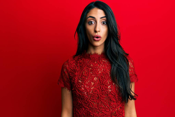 Beautiful hispanic woman wearing elegant clothes over red background scared and amazed with open mouth for surprise, disbelief face  - Photo, Image