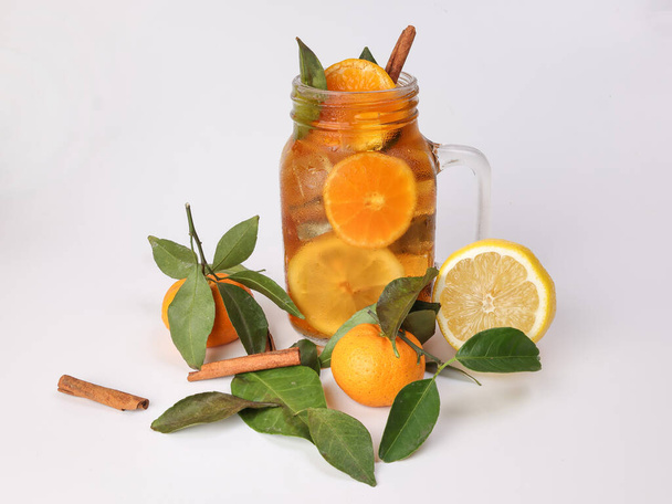 Chá de laranja de limão de gelo líquido com vara de canela de folha verde em caneca de vidro transparente no fundo branco fruta inteira - Foto, Imagem