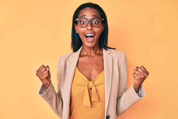 Young african american woman wearing business clothes celebrating surprised and amazed for success with arms raised and open eyes. winner concept.  - Photo, Image