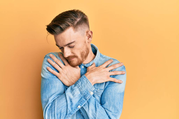 Young redhead man wearing casual denim shirt hugging oneself happy and positive, smiling confident. self love and self care  - Photo, Image
