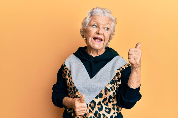 Senior mulher de cabelos grisalhos vestindo sportswear apontando polegar até o lado sorrindo feliz com a boca aberta  - Foto, Imagem