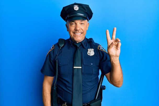 Красивый зрелый мужчина средних лет в полицейской форме улыбается, глядя в камеру, показывая пальцы, делающие знак победы. Номер два.  - Фото, изображение