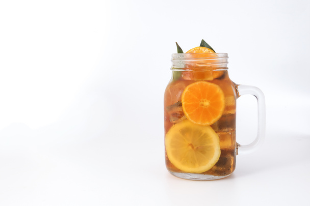 Υγρό παγωμένο τσάι λεμονιού πορτοκαλί με φέτα πράσινο φύλλο κανέλα ραβδί σε διαφανές γυάλινο βάζο κούπα σε λευκό φόντο - Φωτογραφία, εικόνα