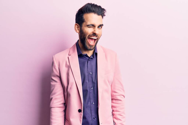 Young handsome man with beard wearing elegant jacket winking looking at the camera with sexy expression, cheerful and happy face.  - Photo, Image