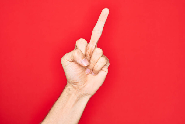 Mano de joven caucásico mostrando los dedos sobre fondo rojo aislado mostrando gesto provocativo y grosero haciendo joder símbolo con el dedo medio
 - Foto, Imagen