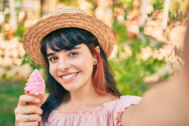 Junge hispanische Touristin im Sommer-Look isst Eis und macht Selfie mit der Kamera im Park. - Foto, Bild