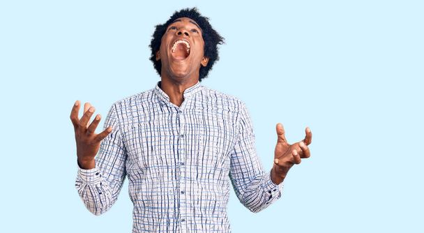 Handsome african american man with afro hair wearing casual clothes crazy and mad shouting and yelling with aggressive expression and arms raised. frustration concept.  - Fotografie, Obrázek