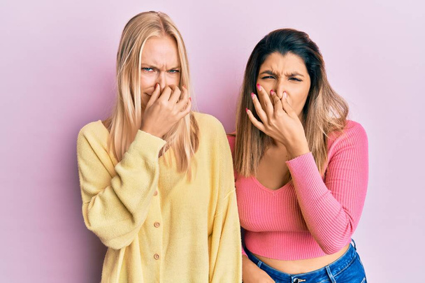 Zwei Freunde, die zusammen vor rosa Hintergrund stehen und etwas Stinkendes und ekelhaften, unerträglichen Geruch riechen, halten den Atem mit den Fingern auf der Nase an. schlechter Geruch  - Foto, Bild