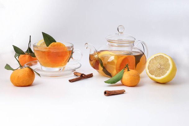 Liquid tea lemon orange slice green leaf cinnamon stick in transparent glass teacup saucer teapot kettle on white background - Photo, Image
