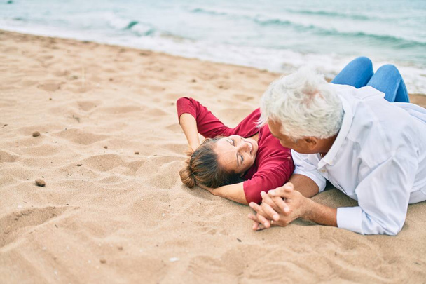 Влюбленная пара среднего возраста, лежащая на песке на пляже счастливая и весёлая вместе - Фото, изображение
