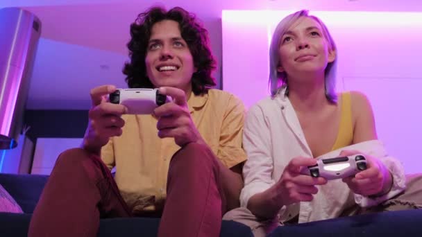 Χαμογελώντας ζευγάρι κρατώντας gamepads παίζοντας βιντεοπαιχνίδι στο σπίτι. Χαμηλή γωνία λήψης των νέων που περνούν χρόνο μαζί κατά τη διάρκεια της απομόνωσης σε πανδημία. - Πλάνα, βίντεο