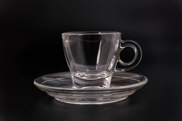 Vidrio transparente vacío ver a través de taza de té de café platillo sobre fondo negro - Foto, imagen