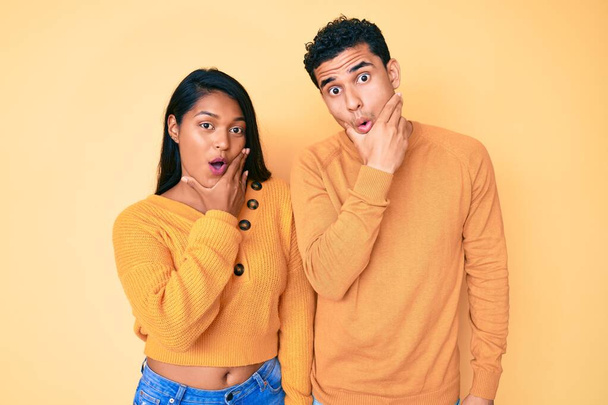 Beautiful latin young couple wearing casual clothes together looking fascinated with disbelief, surprise and amazed expression with hands on chin  - Foto, Imagen