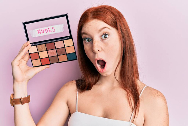 Young red head girl holding blush palette of nudes colors scared and amazed with open mouth for surprise, disbelief face  - Foto, imagen