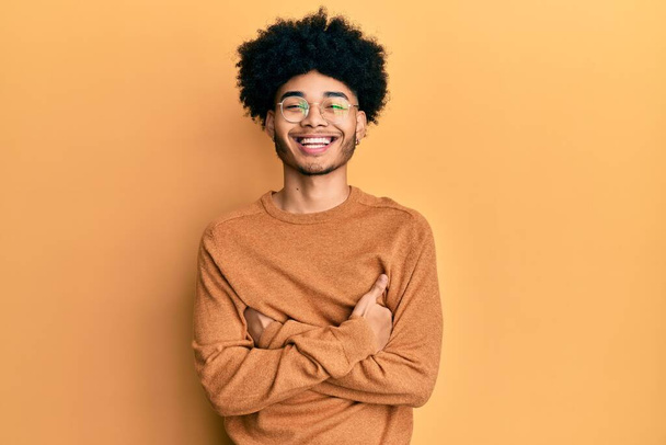 Νεαρός Αφροαμερικάνος με αφρο μαλλιά που φοράει casual χειμωνιάτικο πουλόβερ χαρούμενο πρόσωπο χαμογελώντας με σταυρωμένα χέρια κοιτάζοντας την κάμερα. θετικό πρόσωπο.  - Φωτογραφία, εικόνα