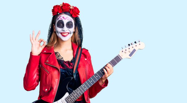 Ölü kostümü giymiş bir kadın elektro gitar çalıyor parmaklarıyla işaret veriyor, gülümseyerek mükemmel bir sembol oluşturuyor.  - Fotoğraf, Görsel