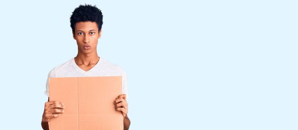 Young african american man holding banner cardboard thinking attitude and sober expression looking self confident  - Photo, Image