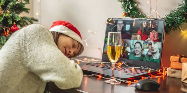 Une jeune femme s'est endormie devant un écran d'ordinateur tout en communiquant avec des amis et des parents par liaison vidéo. Concept pour Noël à distance et fêtes du Nouvel An - Photo, image