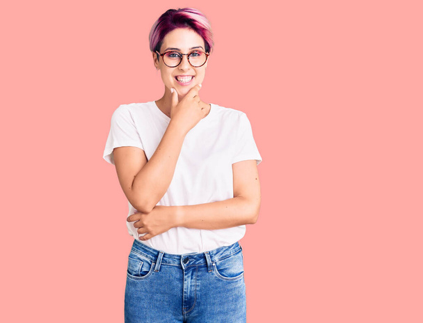 Young beautiful woman with pink hair wearing casual clothes and glasses looking confident at the camera smiling with crossed arms and hand raised on chin. thinking positive.  - Photo, Image