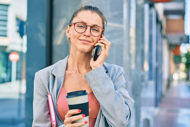 Νεαρή ξανθιά επιχειρηματίας που μιλάει στο smartphone και πίνει καφέ στην πόλη. - Φωτογραφία, εικόνα