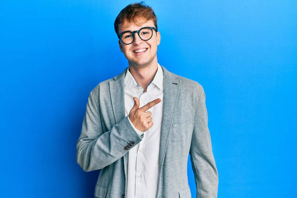 Νεαρός καυκάσιος άνδρας με κομψά ρούχα και γυαλιά χαρούμενος με χαμόγελο στο πρόσωπο που δείχνει με το χέρι και το δάχτυλο στο πλάι με χαρούμενη και φυσική έκφραση στο πρόσωπο  - Φωτογραφία, εικόνα