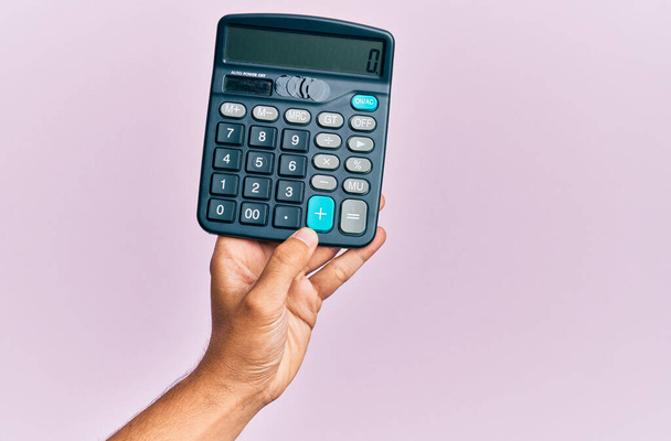 Kéz a fiatal spanyol férfi gazdaság számológép felett elszigetelt rózsaszín háttér. - Fotó, kép
