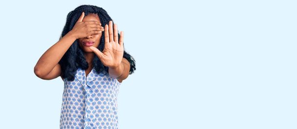 Piękna Afroamerykanka w letniej koszuli zakrywającej dłońmi oczy i wykonująca gest zatrzymania ze smutkiem i strachem. wstydliwa i negatywna koncepcja.  - Zdjęcie, obraz