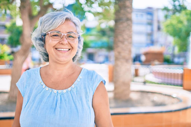 Middelbare leeftijd vrouw met grijs haar glimlachen gelukkig buiten - Foto, afbeelding
