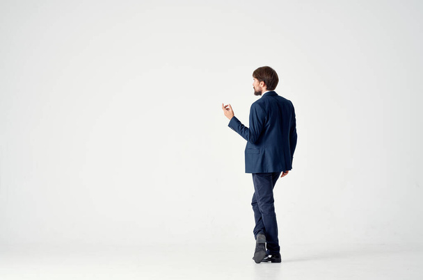 Gentleman in a blue suit gestures with his hands on a light background back view business finance - Foto, afbeelding