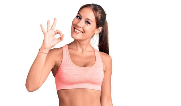 Young beautiful hispanic woman wearing sportswear smiling positive doing ok sign with hand and fingers. successful expression.  - Фото, зображення
