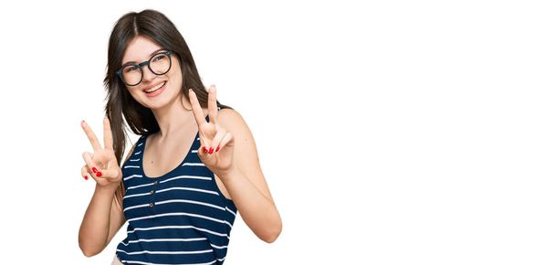 Νεαρή όμορφη καυκάσιος κορίτσι φορώντας casual ρούχα και γυαλιά χαμογελώντας κοιτάζοντας στην κάμερα δείχνει τα δάχτυλα κάνει σημάδι νίκη. Νούμερο δύο..  - Φωτογραφία, εικόνα