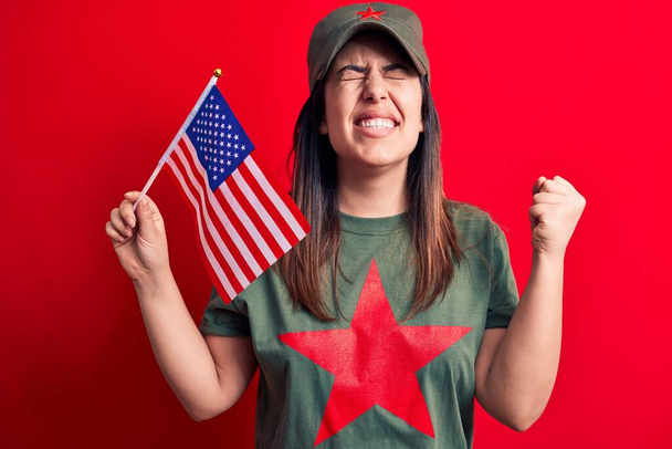 Mulher bonita vestindo camiseta com símbolo comunista estrela vermelha segurando bandeira dos Estados Unidos gritando orgulhoso, celebrando vitória e sucesso muito animado com braço levantado - Foto, Imagem