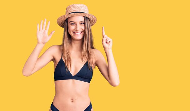 Young beautiful girl wearing bikini and hat showing and pointing up with fingers number six while smiling confident and happy.  - Foto, Bild