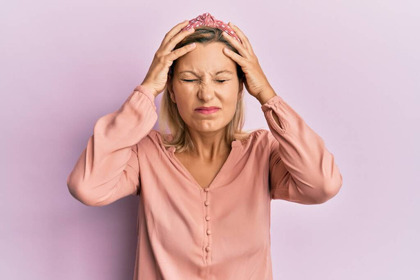 Mujer caucásica de mediana edad que usa ropa casual que sufre de dolor de cabeza desesperada y estresada porque el dolor y la migraña. manos en la cabeza.  - Foto, imagen