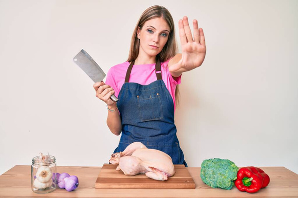 Sarışın, aşçı önlüğü takmış, tavuk pişiriyor, eli açık, dur işareti yapıyor, ciddi ve kendinden emin bir ifadeyle, savunma hareketi yapıyor.  - Fotoğraf, Görsel