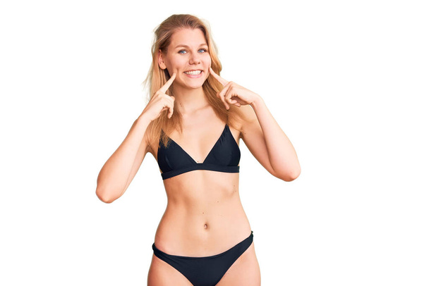 Jeune belle femme blonde portant un bikini souriant avec la bouche ouverte, les doigts pointant et forçant sourire joyeux  - Photo, image