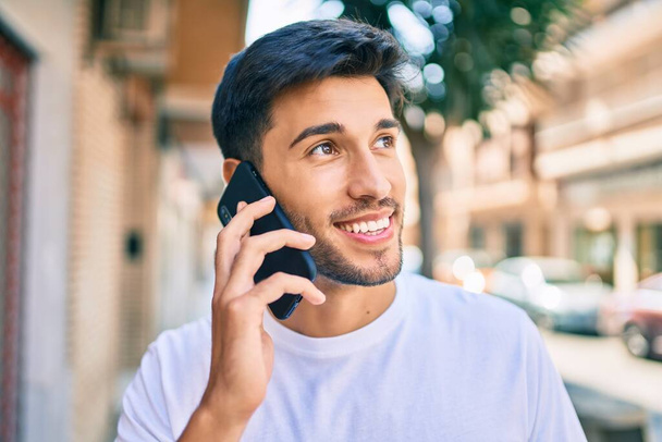Молодий латинський чоловік посміхається щаслива розмова на смартфоні, що йде по місту
. - Фото, зображення