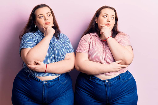 Young plus size twins wearing casual clothes with hand on chin thinking about question, pensive expression. smiling with thoughtful face. doubt concept.  - Photo, Image